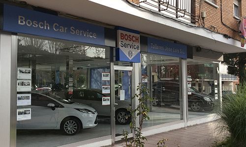 Un taller de Bosch Car Service con ventanales que van desde el suelo hasta el techo, donde se exhiben coches y hay letreros azules.