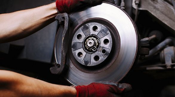 Un mecánico con guantes rojos instala un disco de freno metálico circular en el cubo de un vehículo.