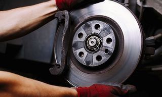 Un mecánico con guantes rojos sostiene el conjunto del disco de freno de un vehículo durante el mantenimiento.