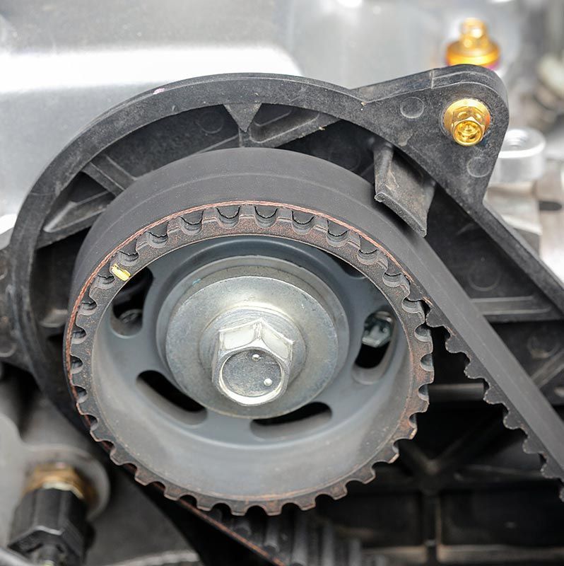 Primer plano de una correa de distribución dentada del motor enrollada alrededor de una polea dentada gris dentro de una carcasa de plástico negro.