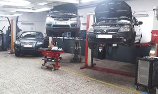 Un taller mecánico bien iluminado con dos coches elevados sobre plataformas hidráulicas y un tercer coche aparcado en el suelo.