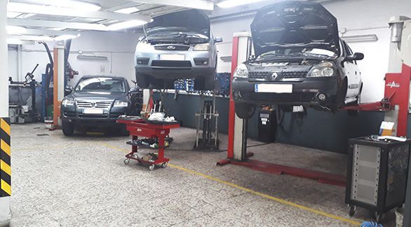 El interior de un taller mecánico con tres coches, dos de ellos elevados sobre plataformas hidráulicas para su mantenimiento.