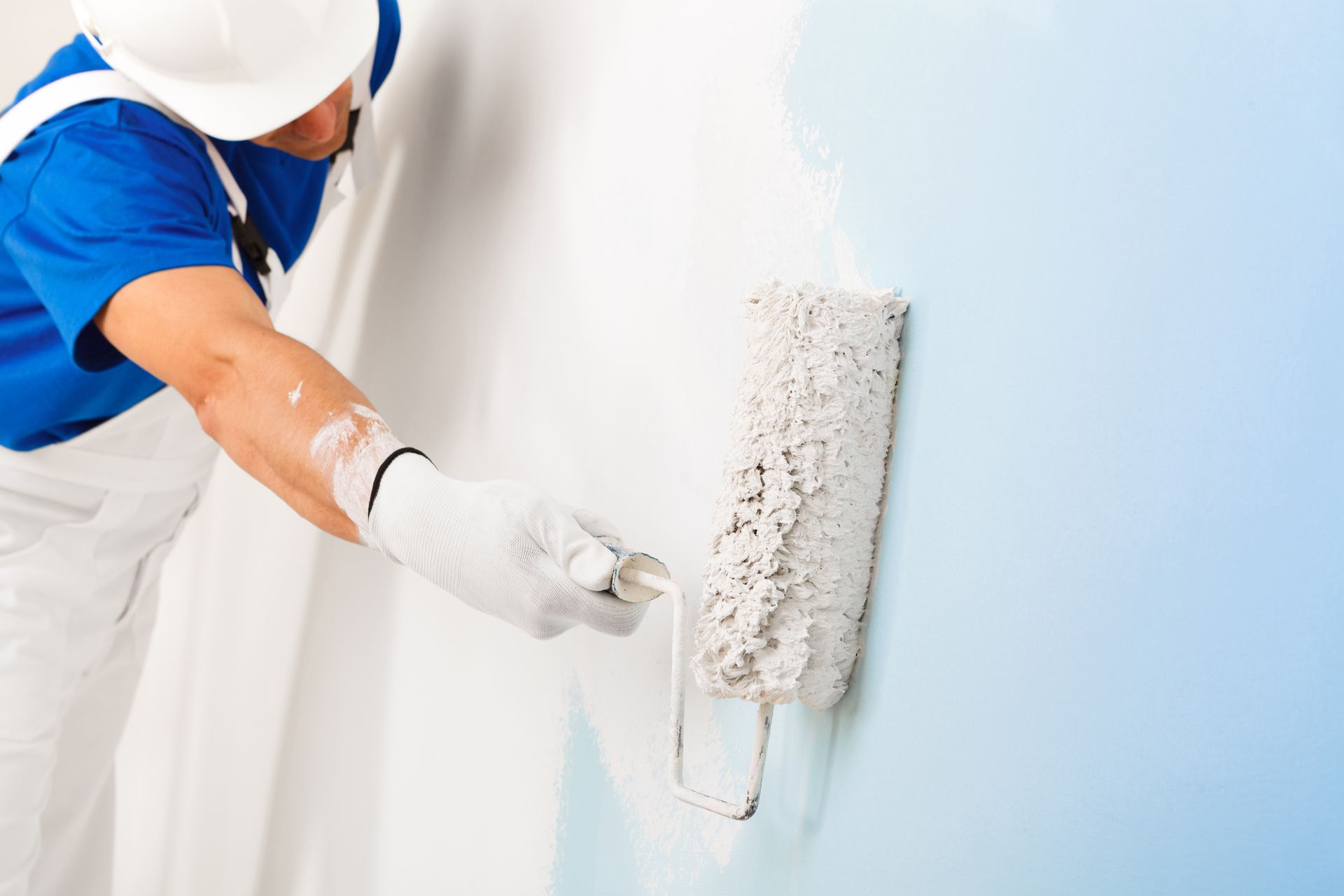 Un peintre applique de la peinture blanche sur un mur bleu clair.