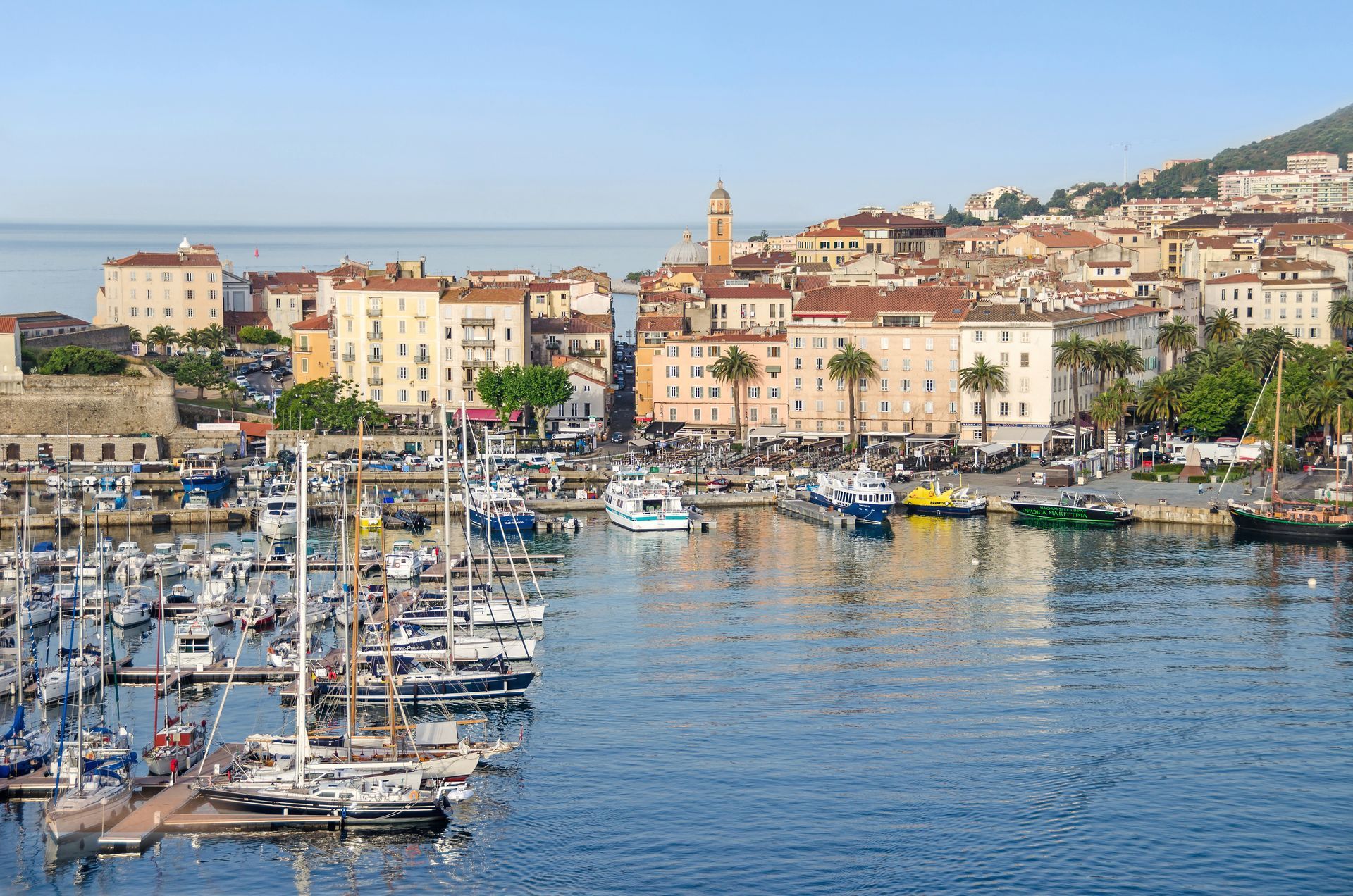 Port avec voiliers et yachts à côté d'une ville côtière aux bâtiments aux couleurs pastel par une journée ensoleillée