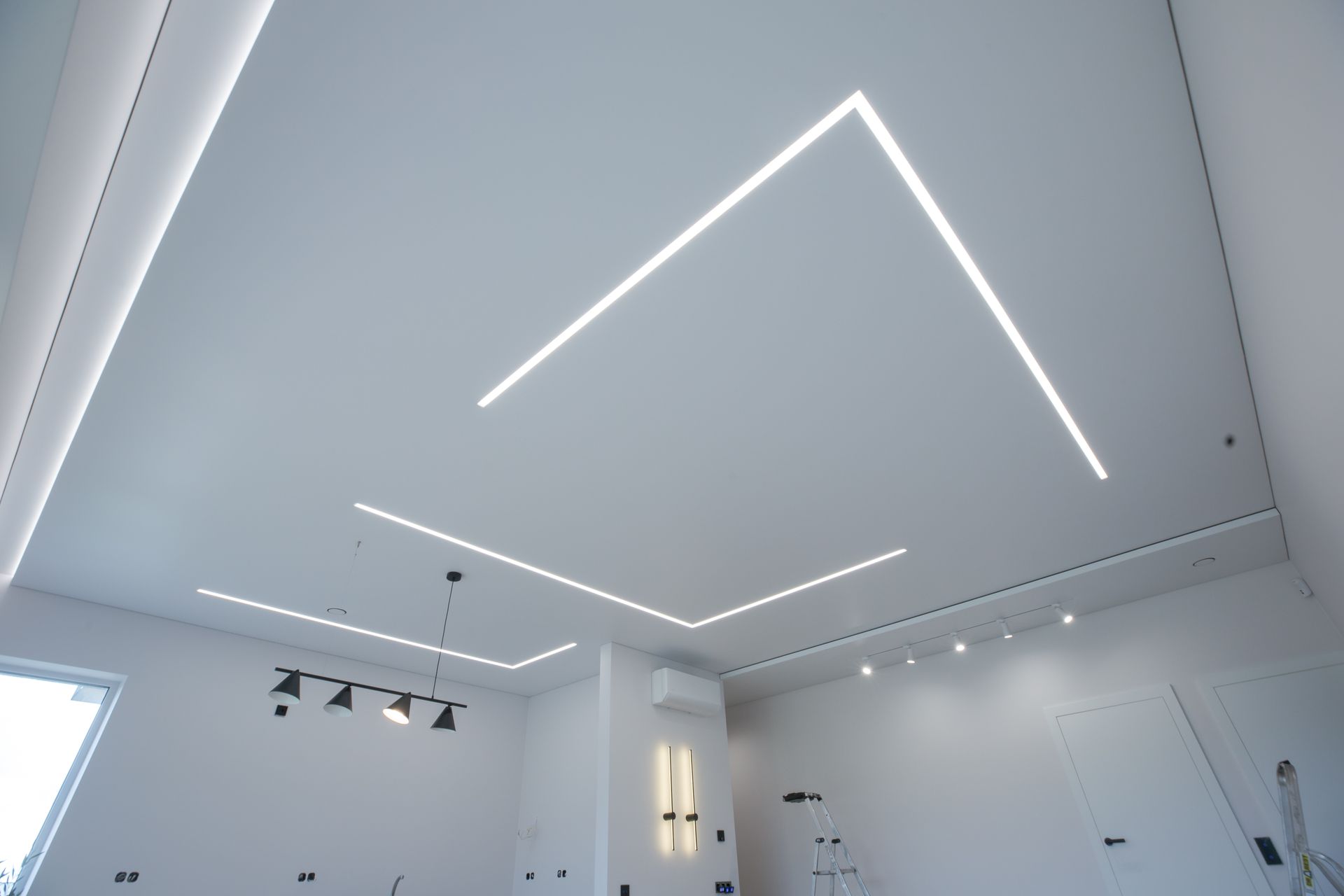 Plafond blanc minimaliste avec lignes lumineuses LED géométriques et spots sur rail en dessous
