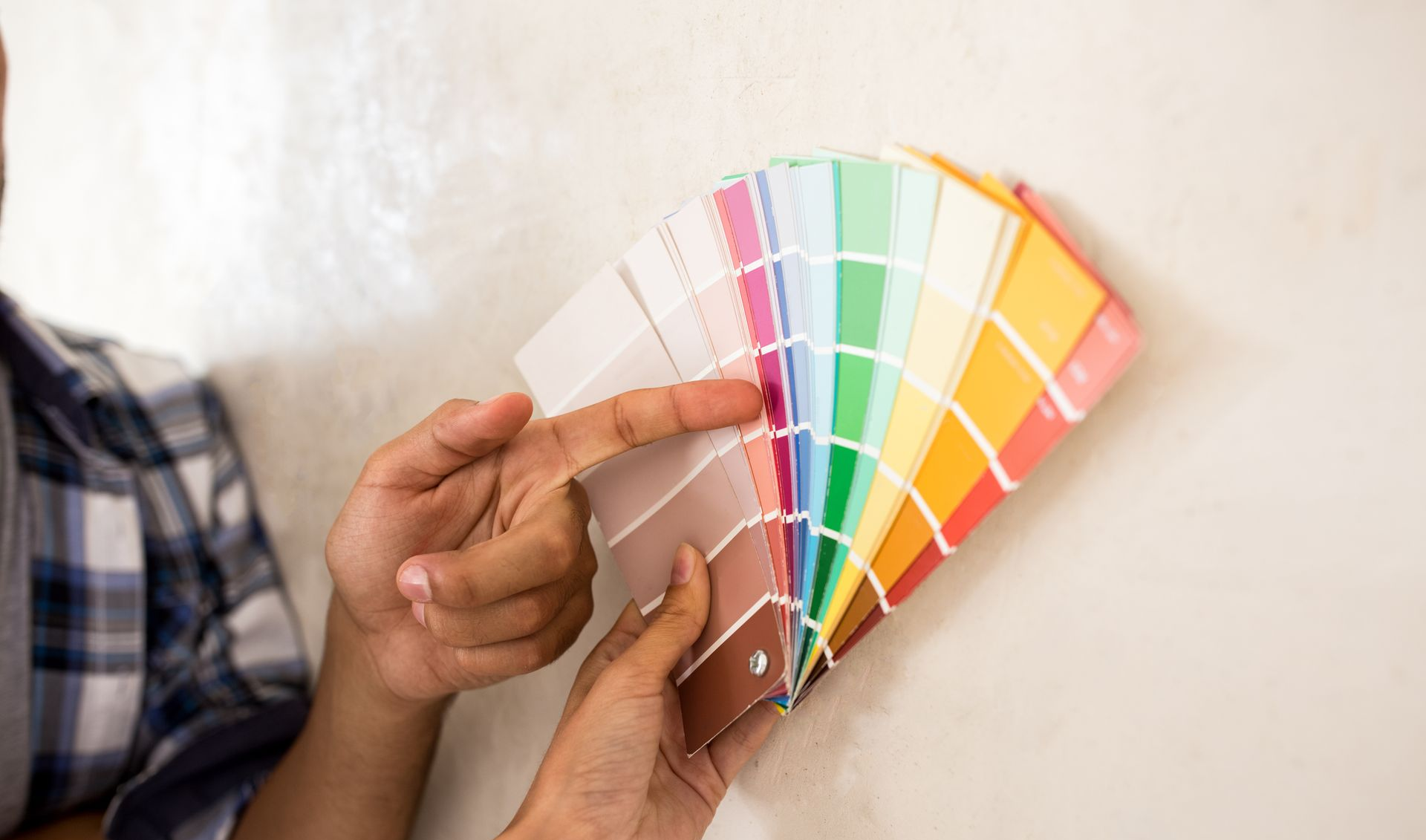 Main tenant un éventail d'échantillons de peinture colorés devant un mur blanc
