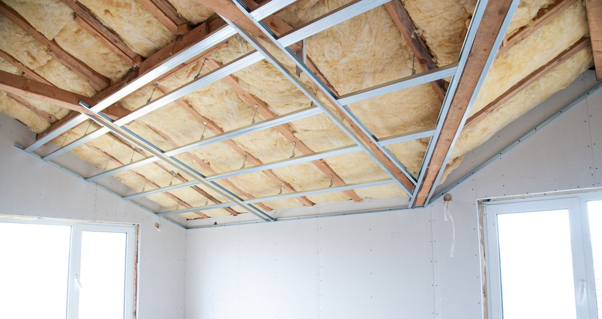 Plafond inachevé avec isolation apparente et ossature métallique au-dessus de murs et fenêtres blancs