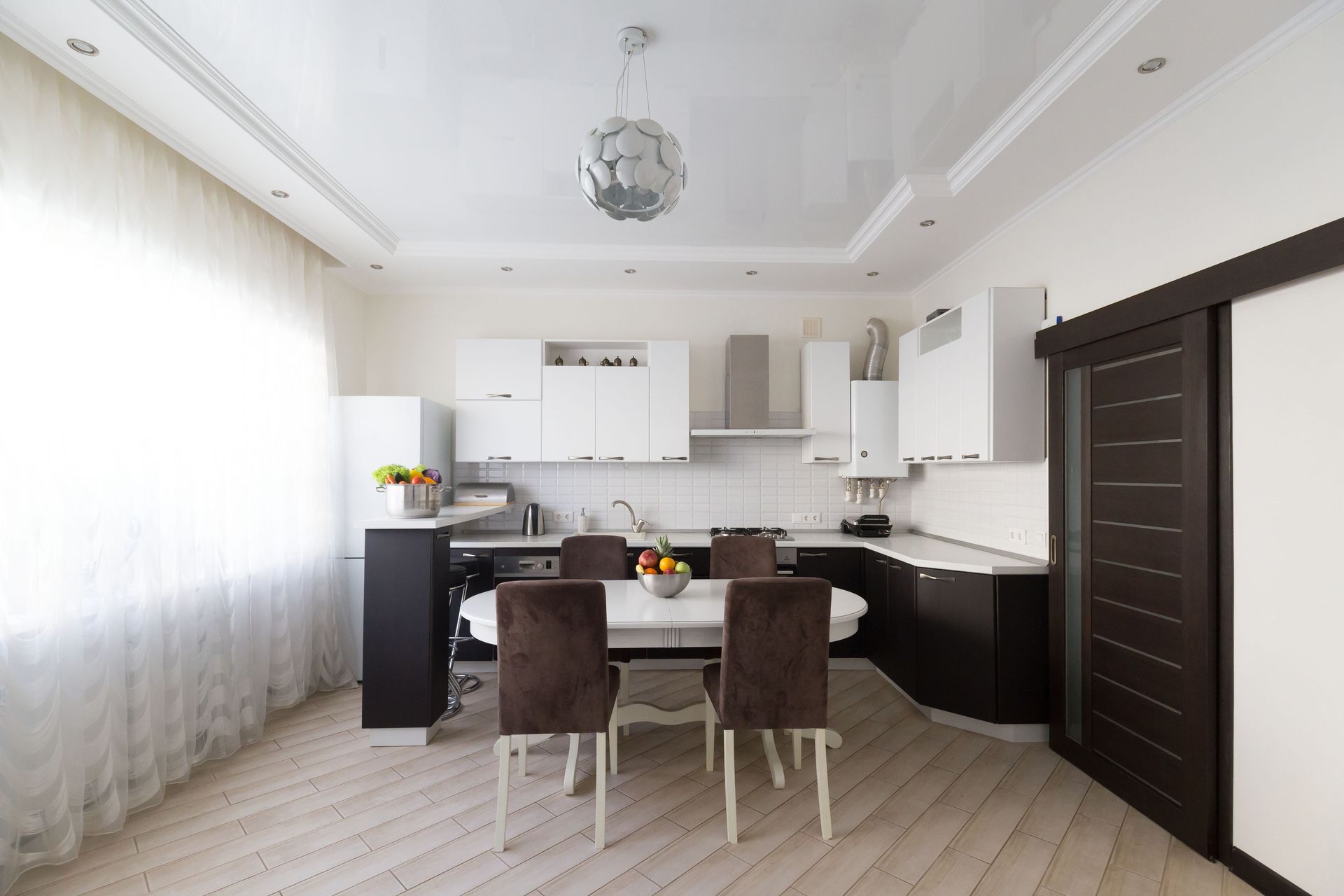 Cuisine et salle à manger modernes blanches avec des touches de bois foncé et des rideaux transparents.