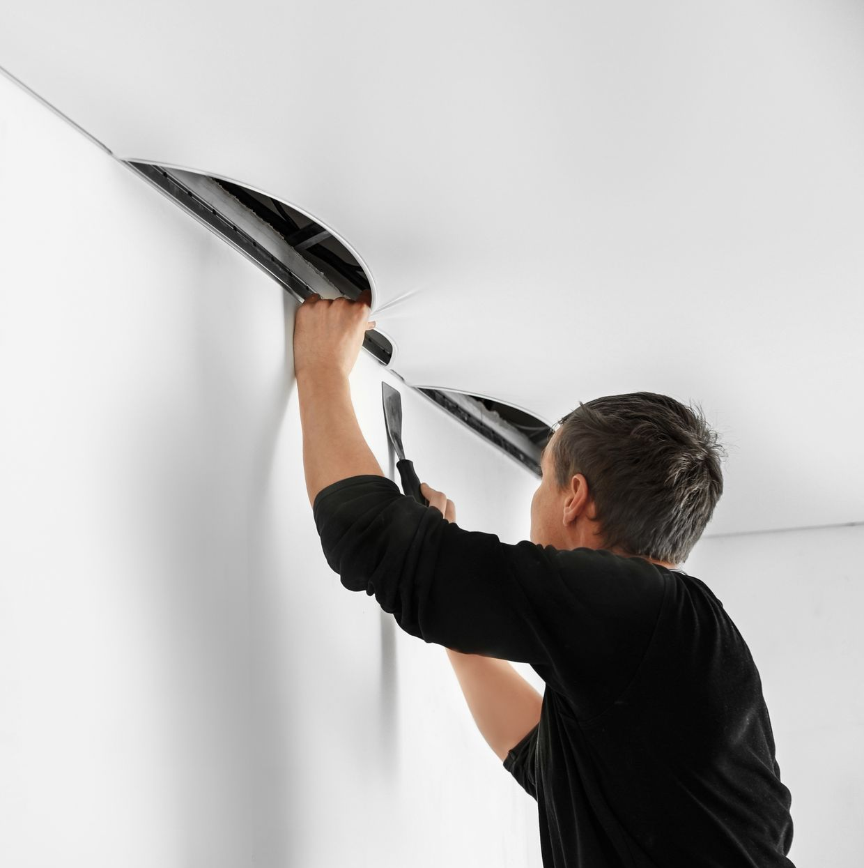 Ouvrier installant des moulures de plafond avec un couteau utilitaire dans une pièce blanche