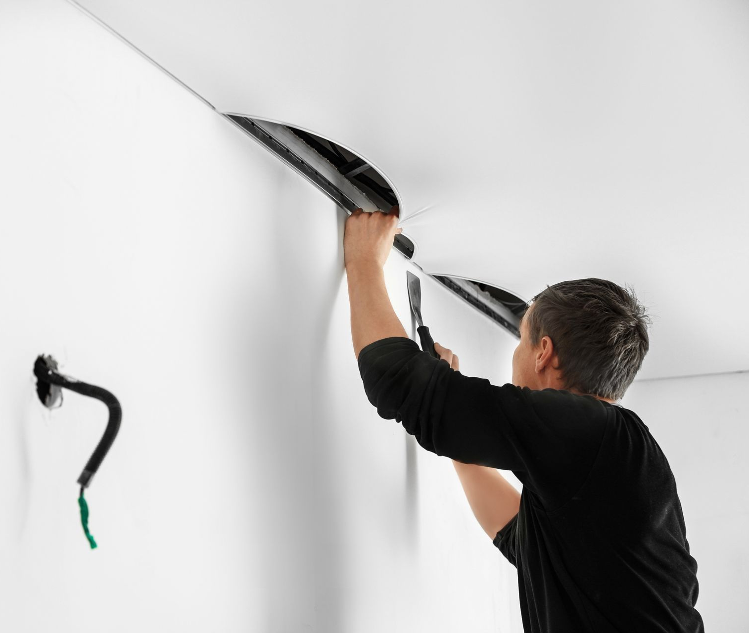 Une personne applique du mastic noir sur un joint de mur blanc à l'aide d'un pistolet à calfeutrer.