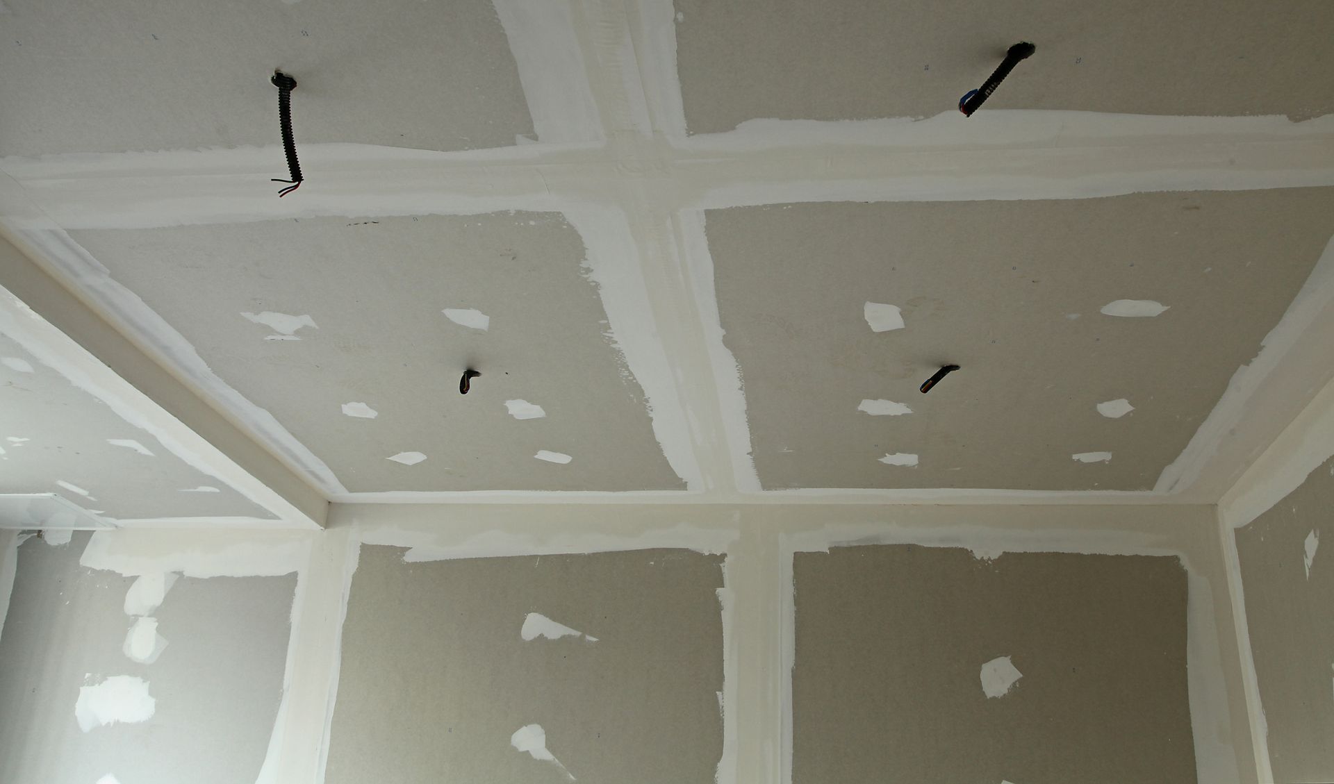 Plafond de pièce partiellement fini avec des plaques de plâtre réparées et des fils électriques suspendus.