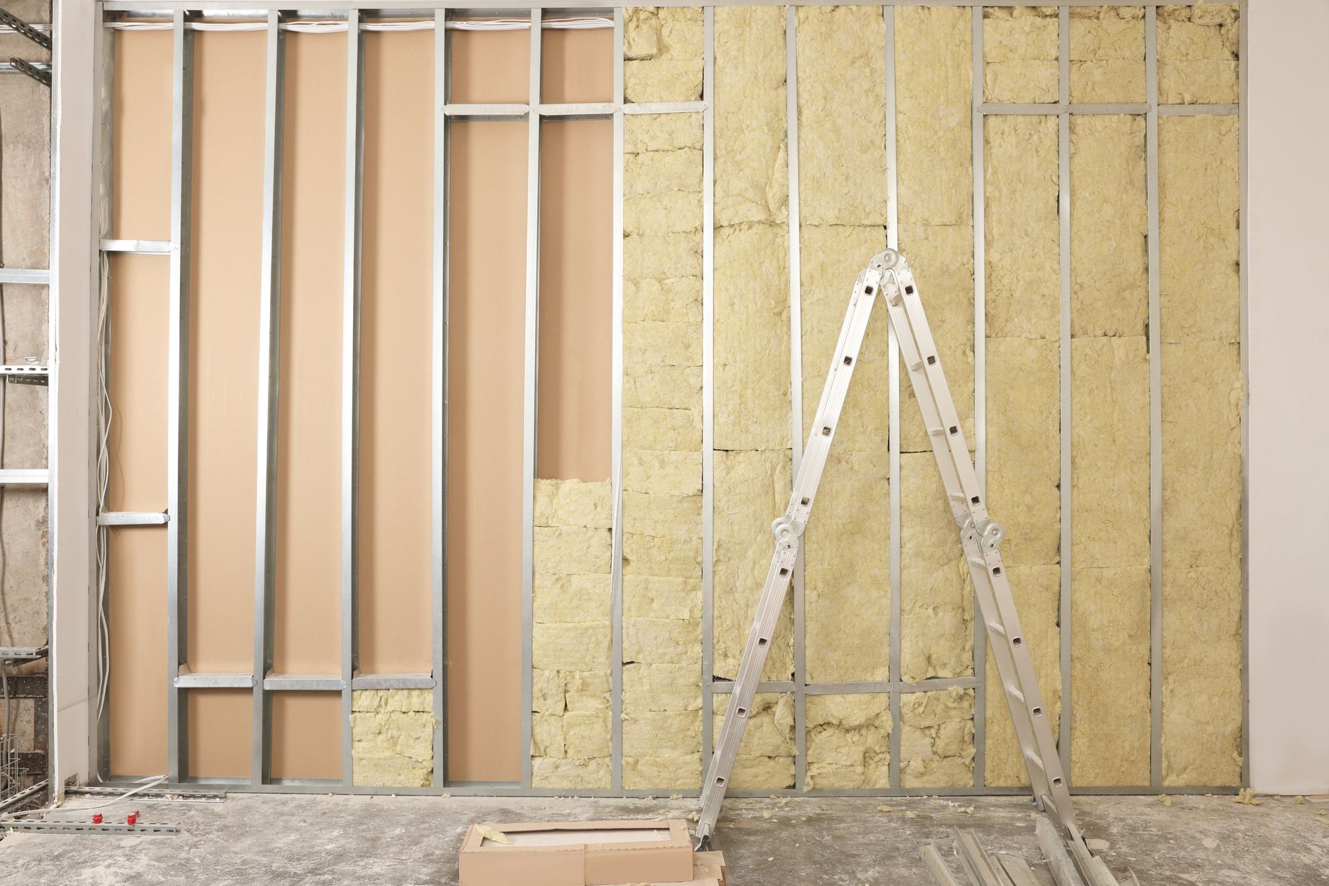 Mur intérieur partiellement construit avec montants apparents, isolation et échelle sur un chantier de construction