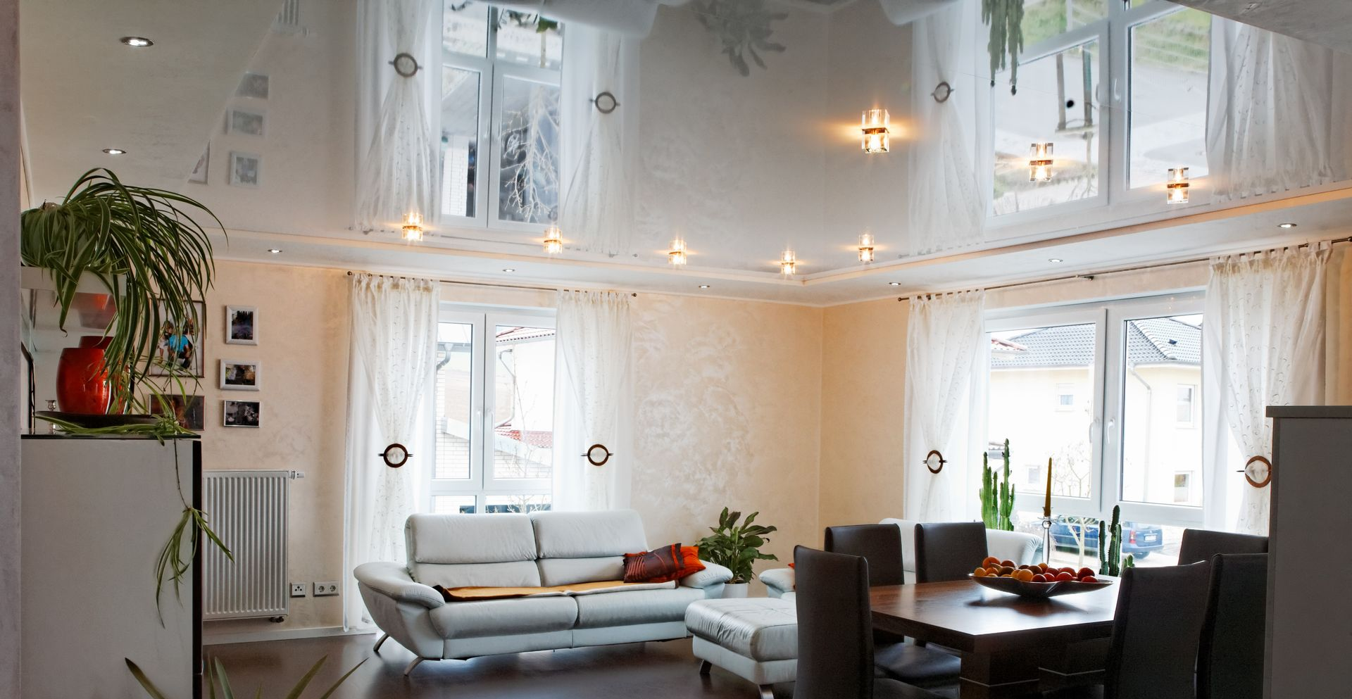 Salon et salle à manger lumineux d'un blanc immaculé, avec canapé, table à manger et grandes fenêtres sous un plafond miroir.