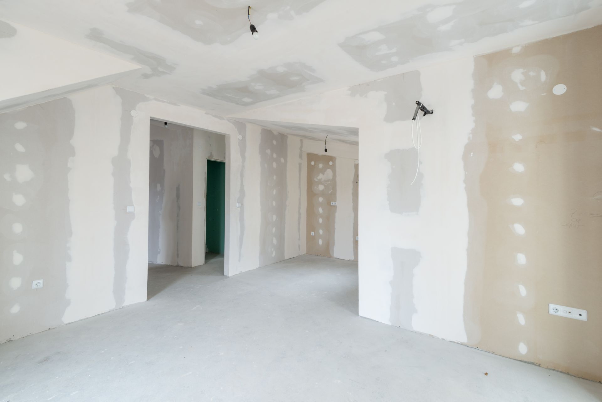 Pièce vide et inachevée, aux murs blancs, cloisons sèches abîmées et sol en béton brut, en cours de rénovation