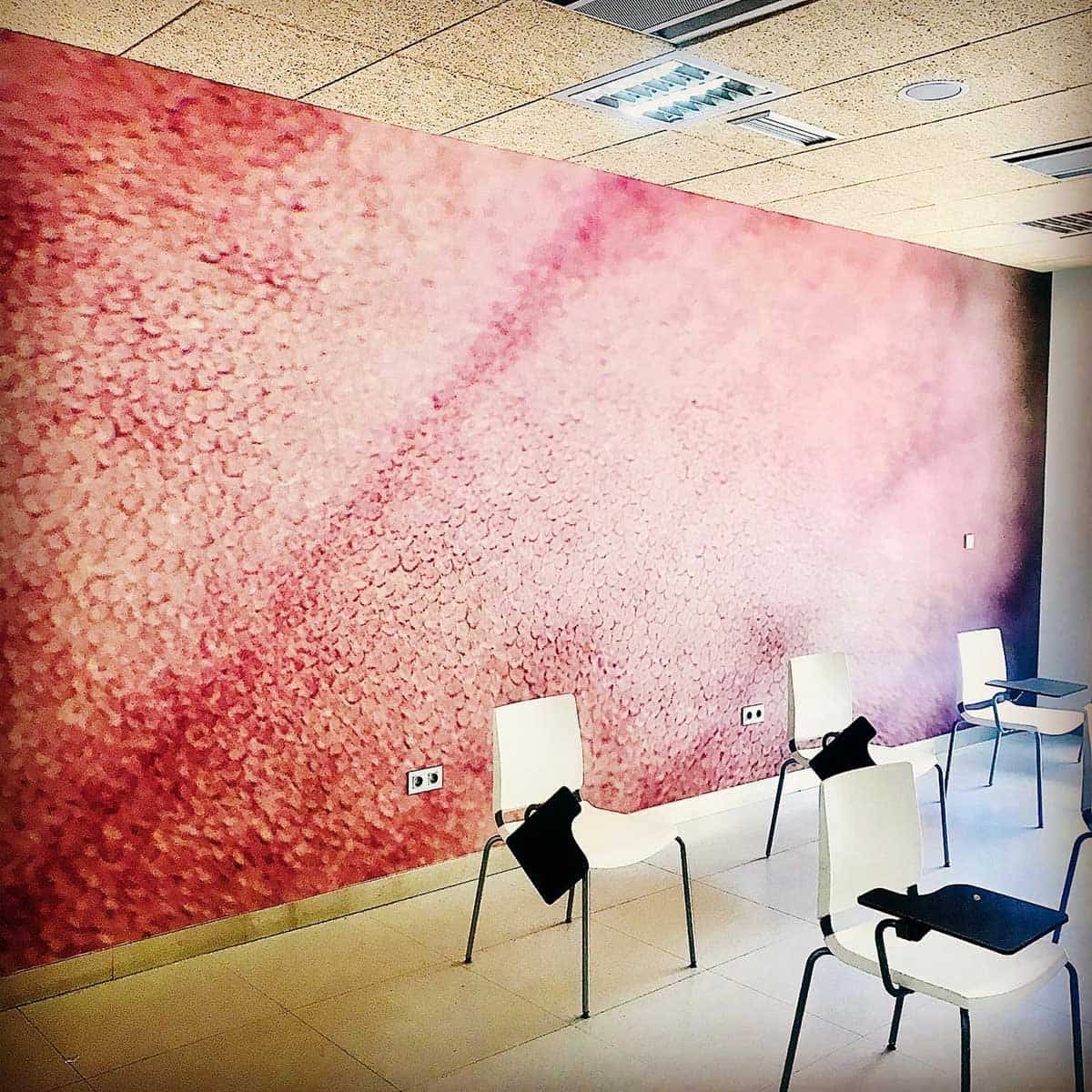 Una sala de conferencias con un gran mural abstracto de color rosa y rojo; sillas blancas en filas.