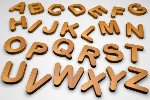 Letras mayúsculas del alfabeto de color dorado dispuestas aleatoriamente sobre una superficie blanca.