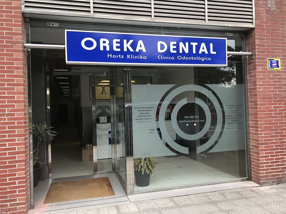 Entrada a la clínica dental Oreka con cartel azul, puertas de cristal y fachada de ladrillo.