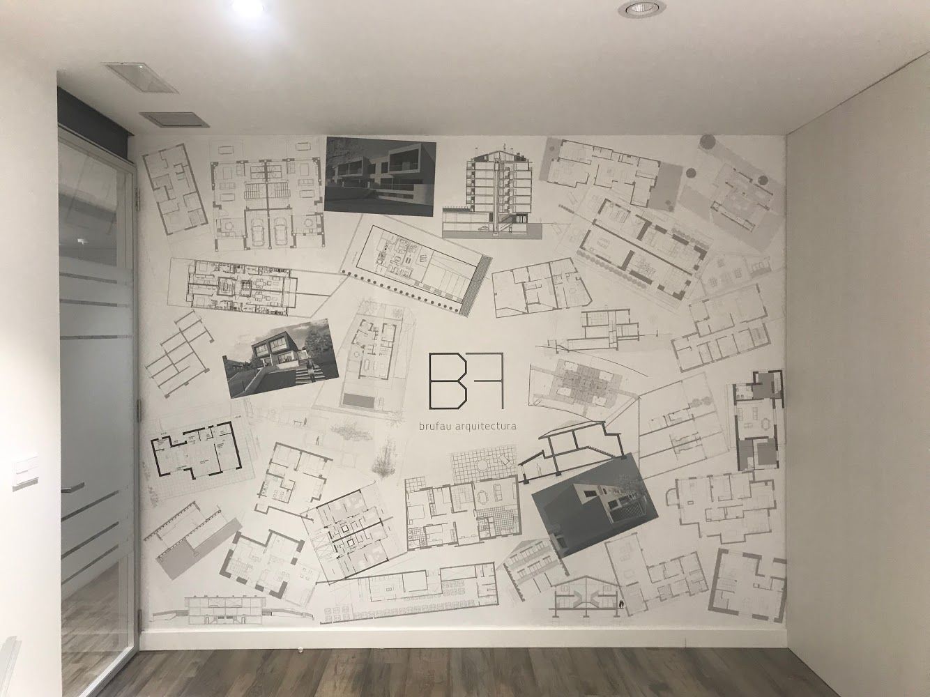 Pared decorada con planos arquitectónicos y logotipo en un espacio de oficina.