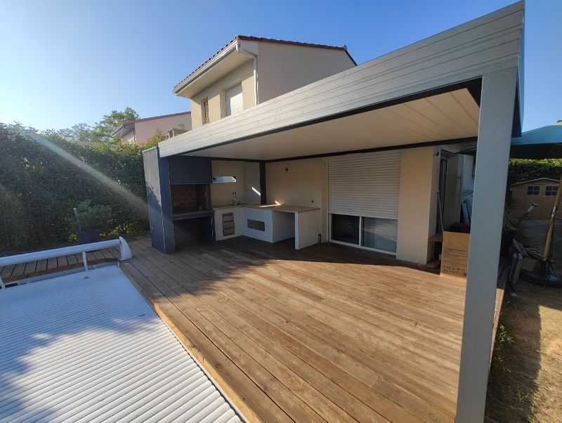 Terrasse extérieure avec plancher en bois, pergola et coin cuisine intégré.