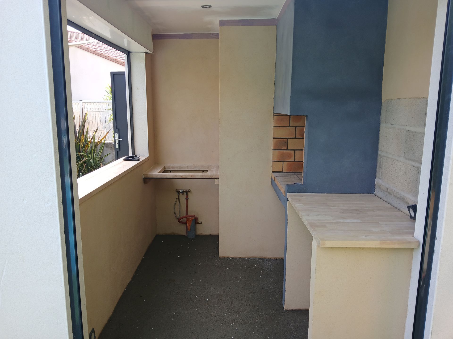 Cuisine extérieure avec évier, plan de travail et four en briques, intégrée dans une structure de couleur claire.