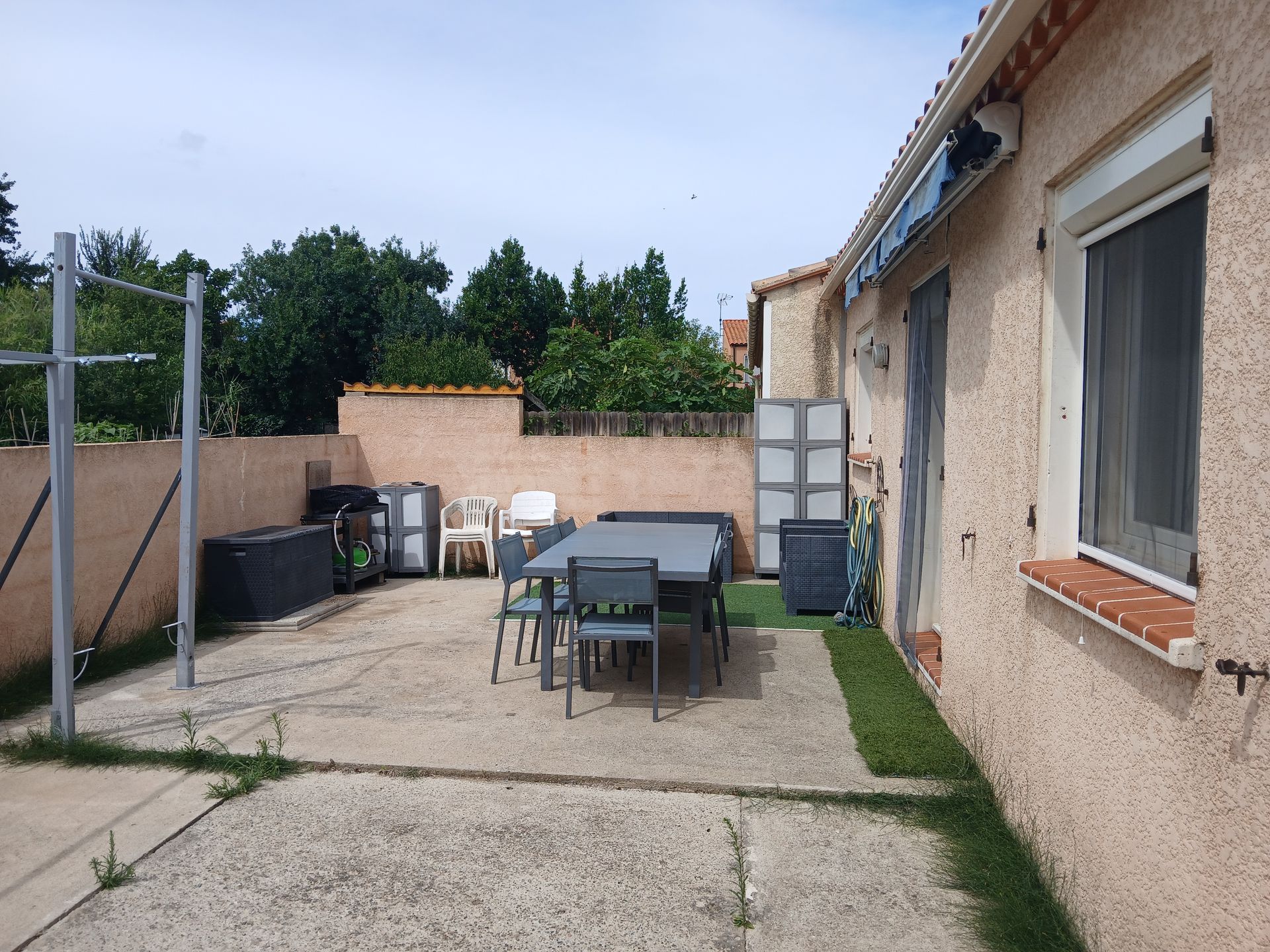 Terrasse avec table, chaises et divers objets à côté d'une maison en stuc.