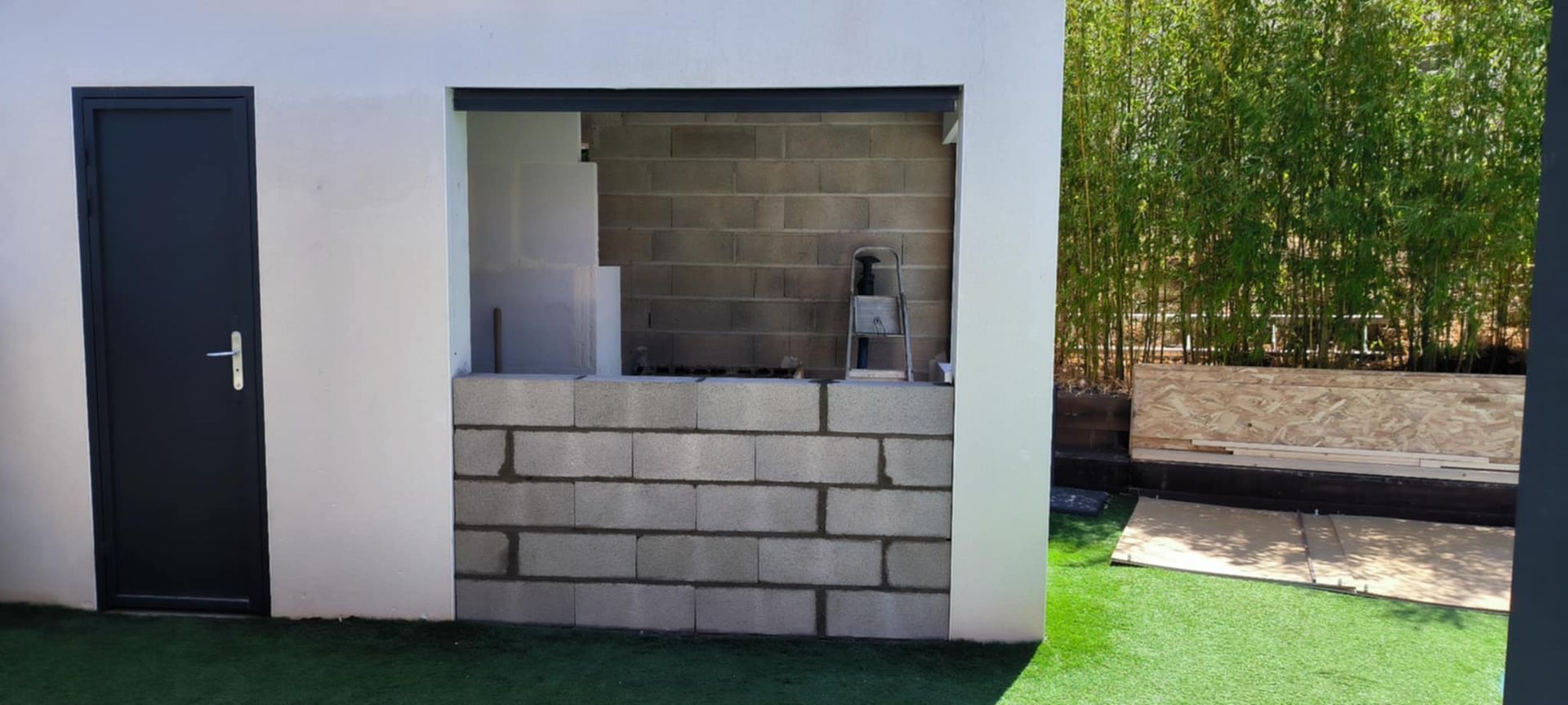 Une structure extérieure partiellement construite avec une base en parpaings, une porte et un fond en bambou.