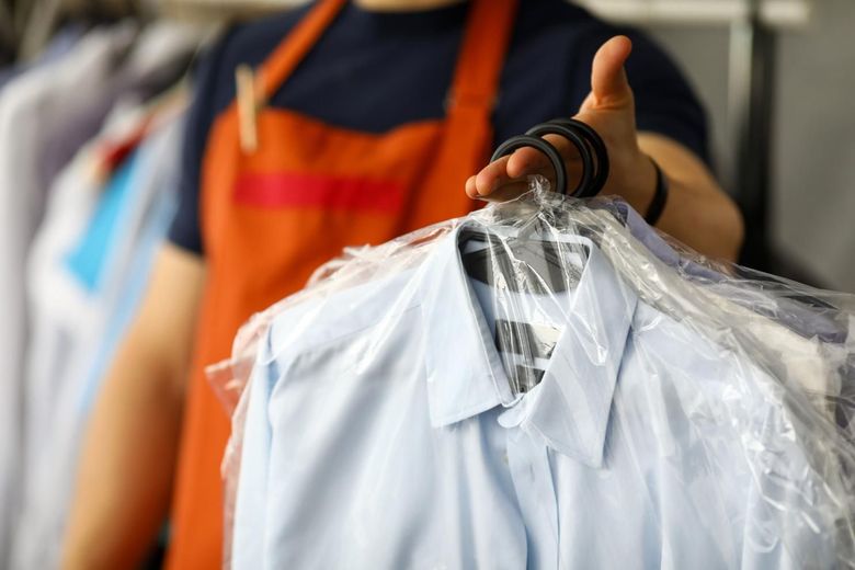 Persona con delantal naranja repartiendo una camisa azul claro en una bolsa de plástico.