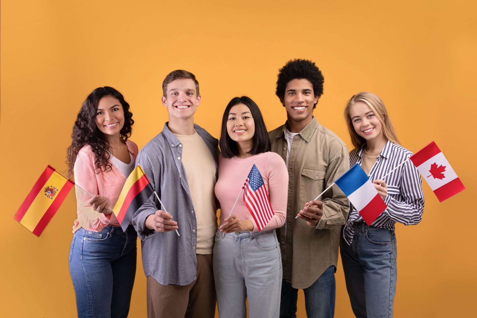 Cinco jóvenes diversos sosteniendo banderas sobre un fondo naranja, sonriendo a la cámara.