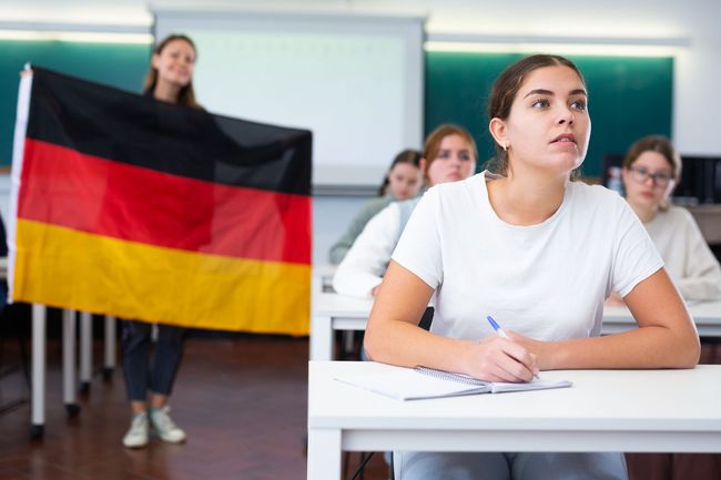 Un estudiante en un aula mira hacia arriba mientras otro sostiene la bandera alemana.