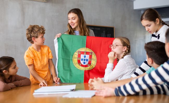 Niños aprendiendo sobre Portugal; la maestra sostiene la bandera portuguesa.