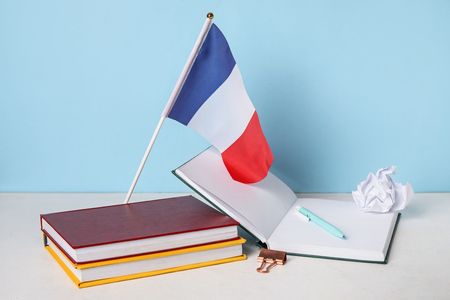 Bandera francesa encima de un cuaderno abierto y libros, con un bolígrafo, papel arrugado, sobre un escritorio.