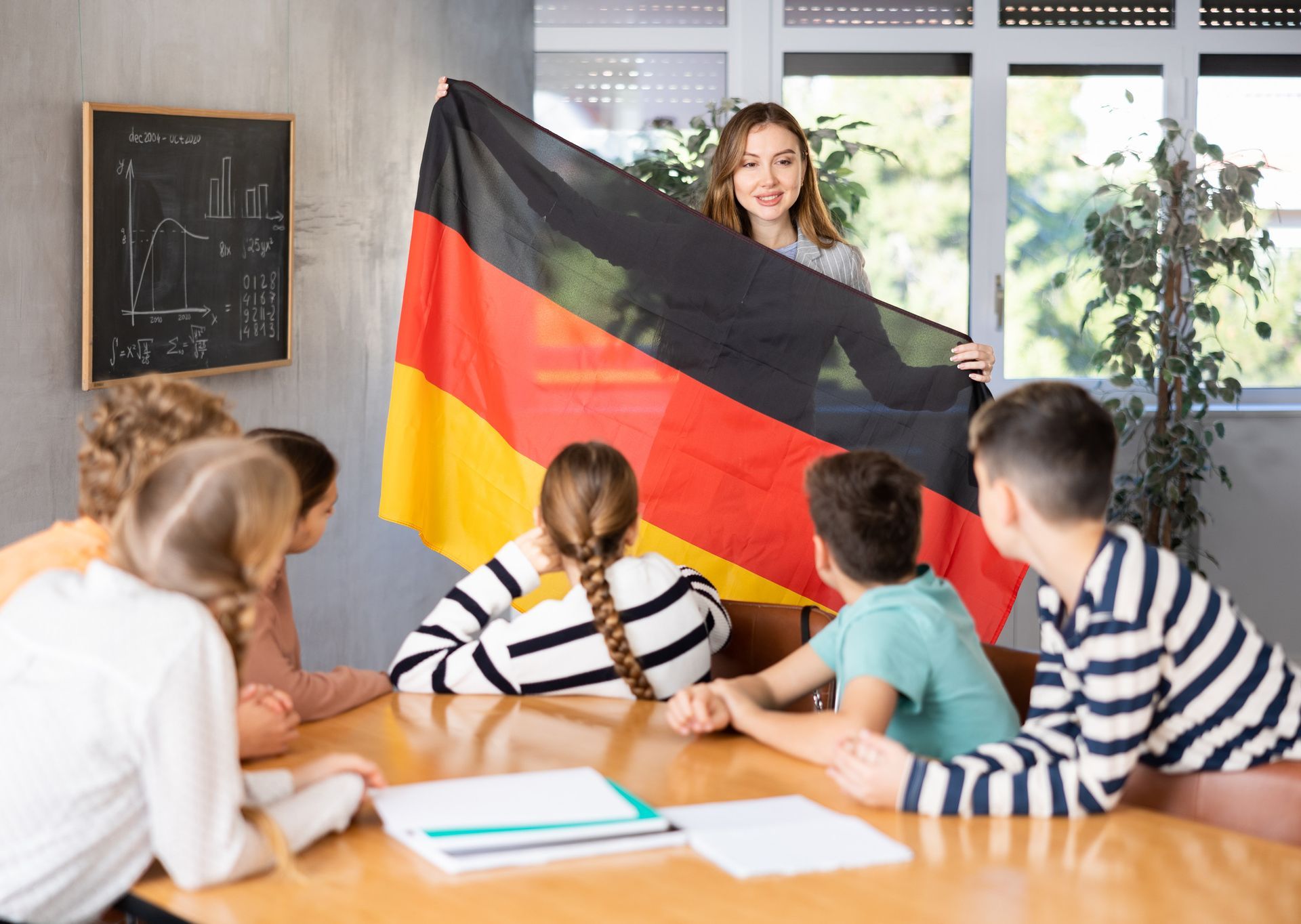 Profesor sosteniendo una bandera alemana y mostrándosela a los estudiantes en un aula.