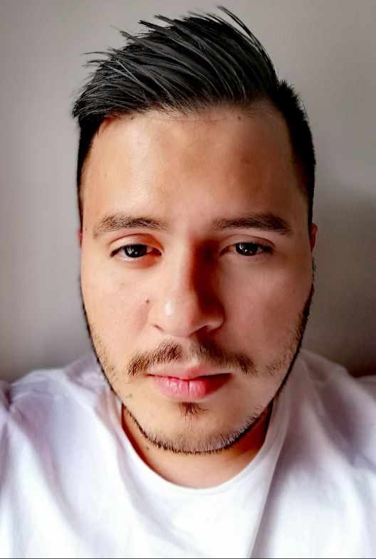 Hombre con cabello oscuro y barba incipiente mirando a la cámara, vistiendo una camisa blanca.