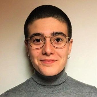 Una persona con cabello corto oscuro y gafas que viste un cuello alto gris sonríe a la cámara.