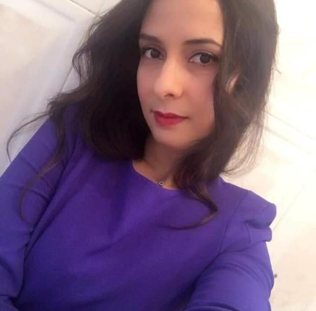 Mujer con cabello oscuro y lápiz labial rojo con un top morado; selfie en primer plano.