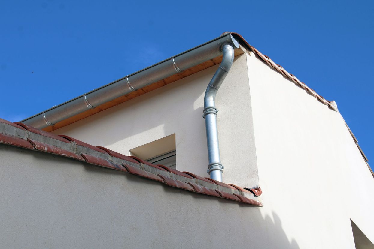 Coin d'une maison aux murs blancs avec une gouttière en zinc.