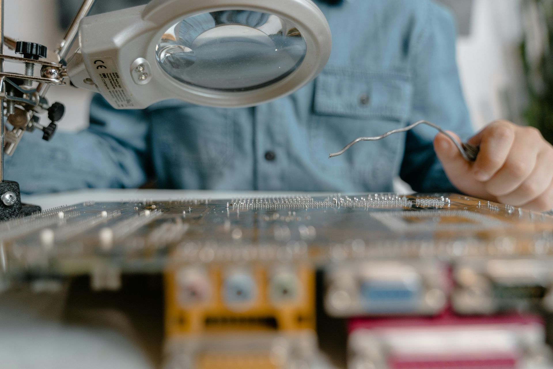 Un technicien inspecte une carte de circuit imprimé à l'aide d'une lampe loupe dans un atelier.
