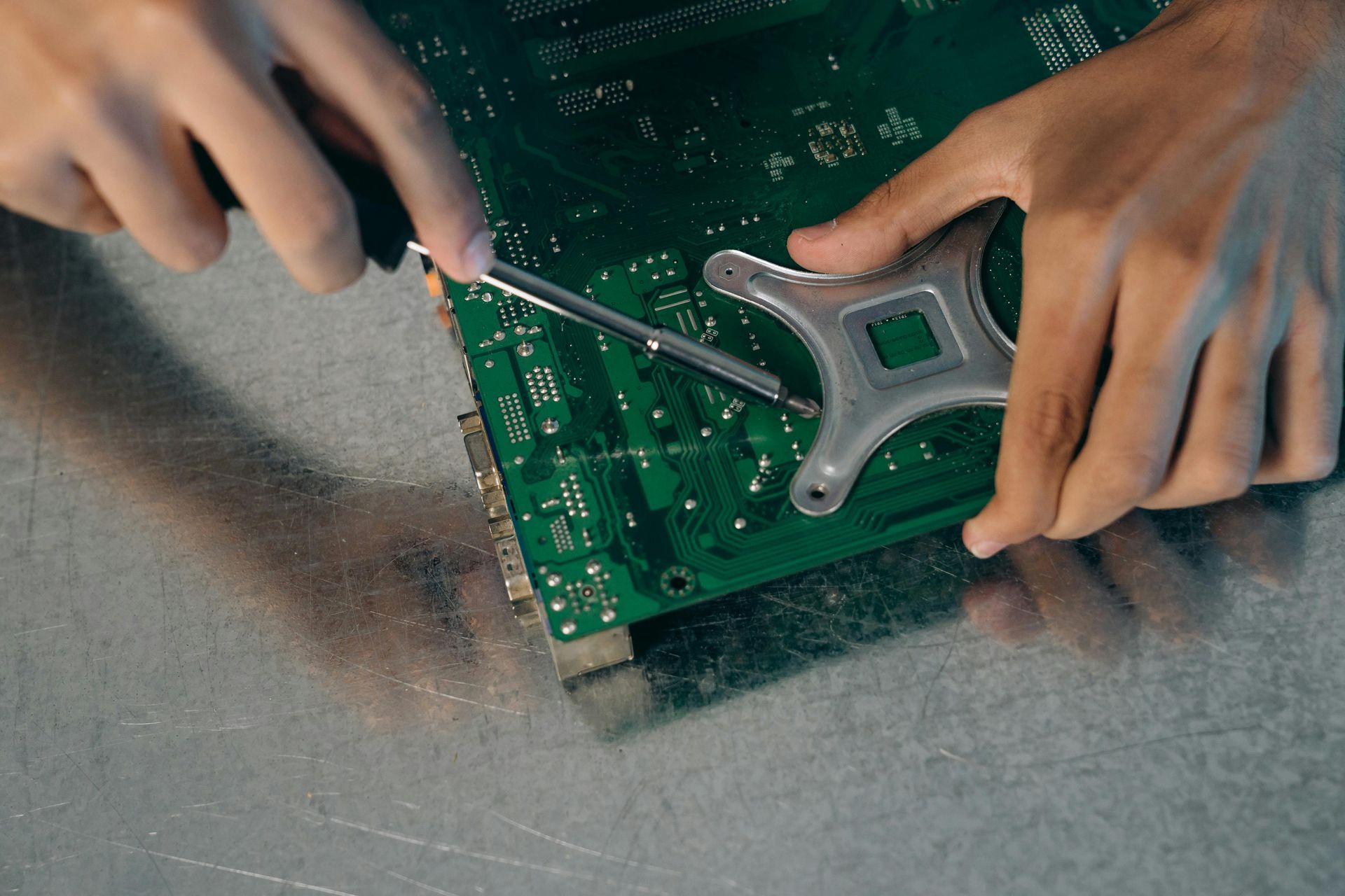 Des mains utilisent un tournevis pour réparer une carte de circuit imprimé verte sur un établi.