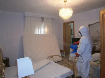 Persona con traje de protección rociando un dormitorio para controlar plagas.