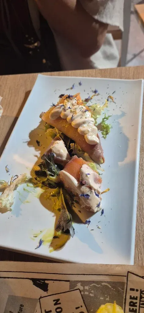 Sobre una mesa de madera reposa un plato de comida con varios trozos de pescado, aderezado con salsa y verduras.