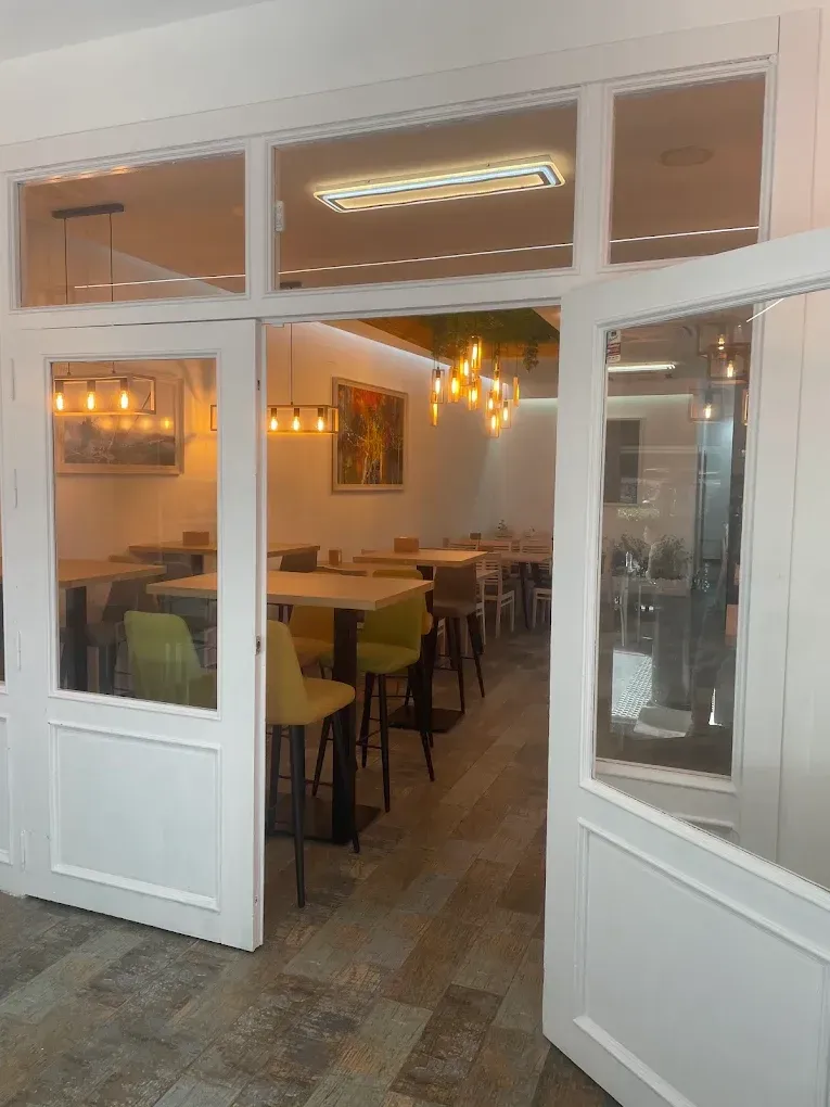 Interior de restaurante con puertas abiertas, mesas, sillas e iluminación cálida.