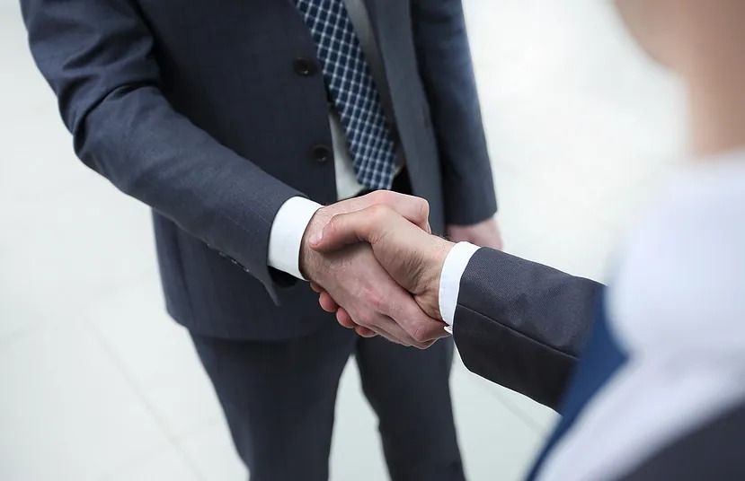 Dos empresarios se dan la mano, primer plano. Uno lleva traje azul marino y corbata estampada.