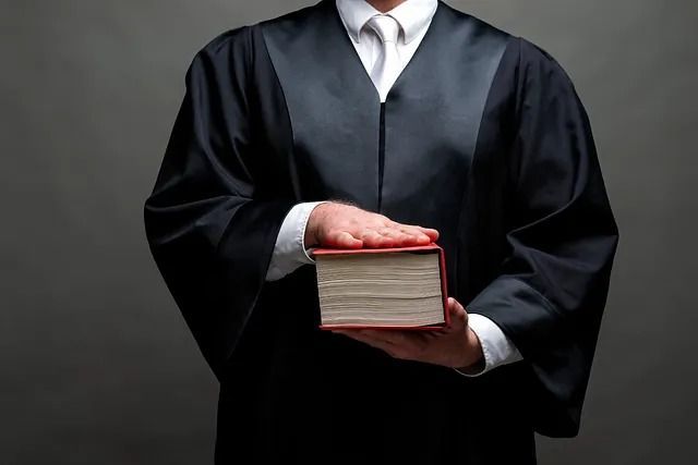 Persona con toga judicial sosteniendo un libro y con la mano levantada como si estuviera haciendo juramento.