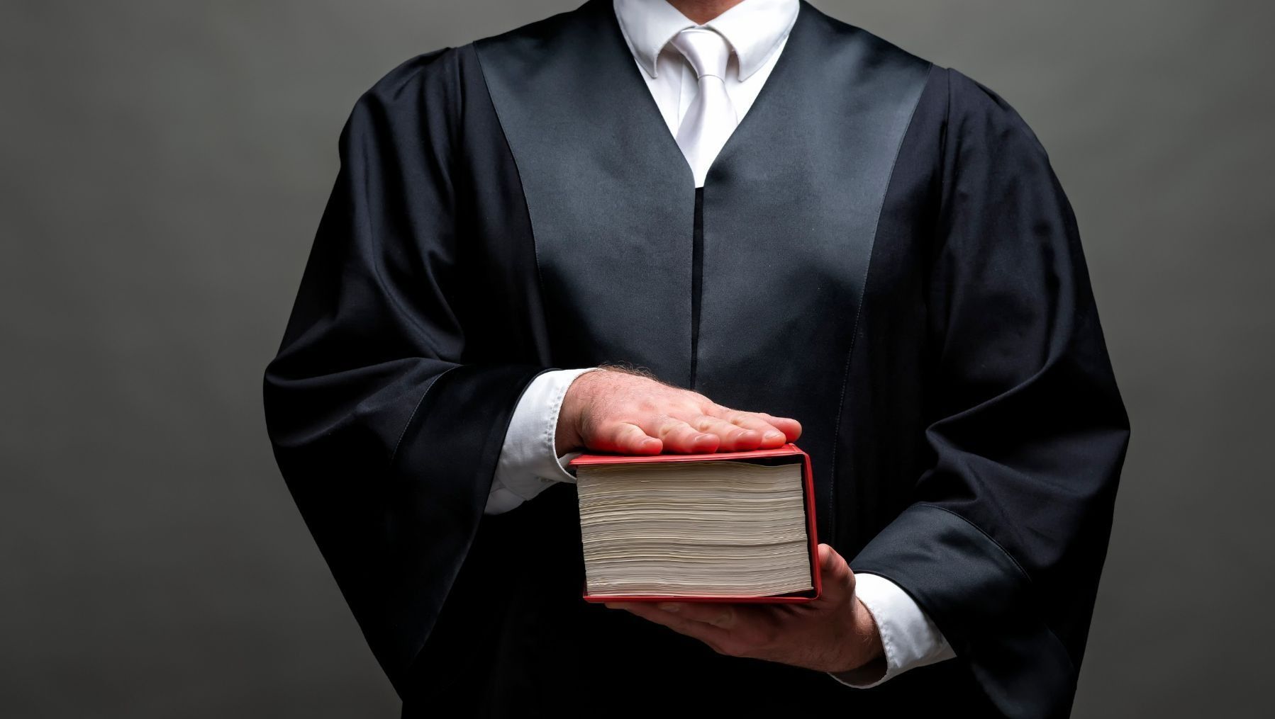 Persona con toga judicial prestando juramento, con la mano sobre un libro grueso.