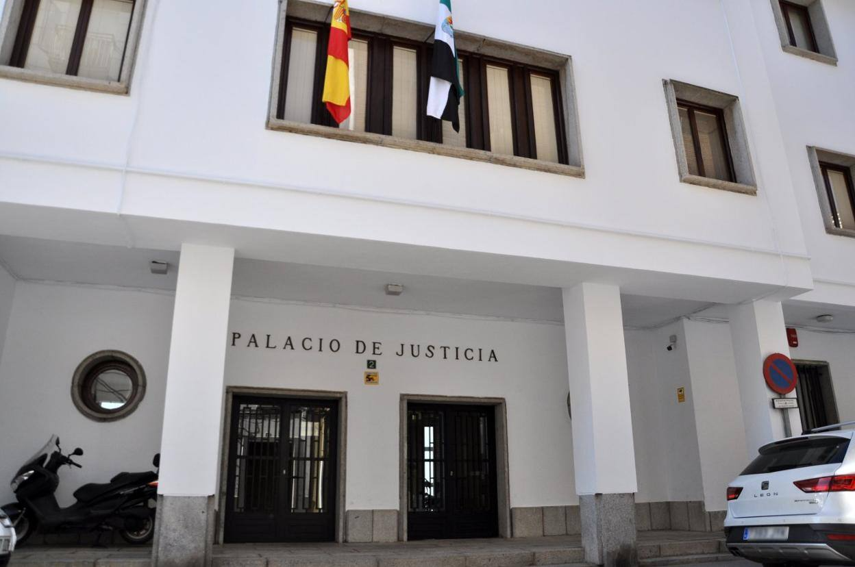 Edificio del Palacio de Justicia con banderas españolas, una scooter y un coche aparcado.