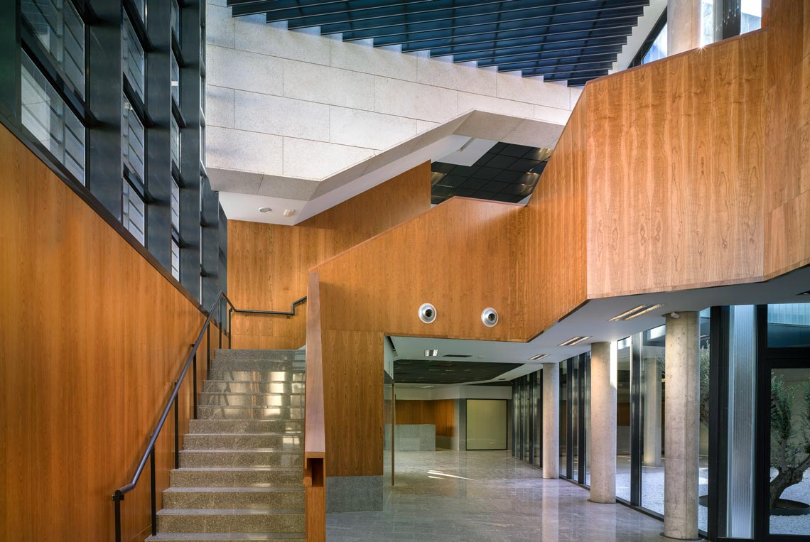 Interior con paneles de madera, escalera y grandes ventanales.