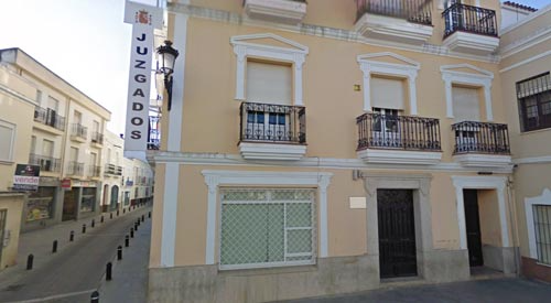 Vista de un edificio amarillo claro con balcones; se ve el cartel de