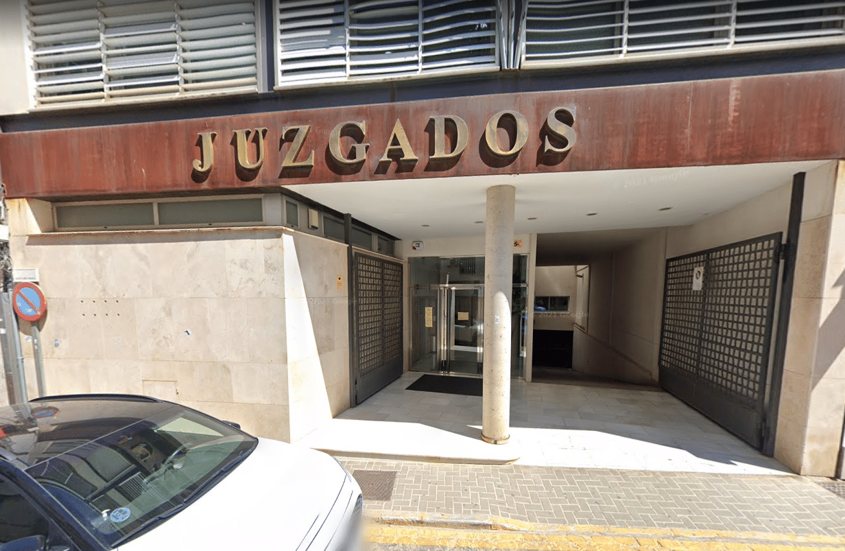 Entrada al edificio de los Juzgados, palacio de justicia español, con letras doradas encima y un coche aparcado delante.