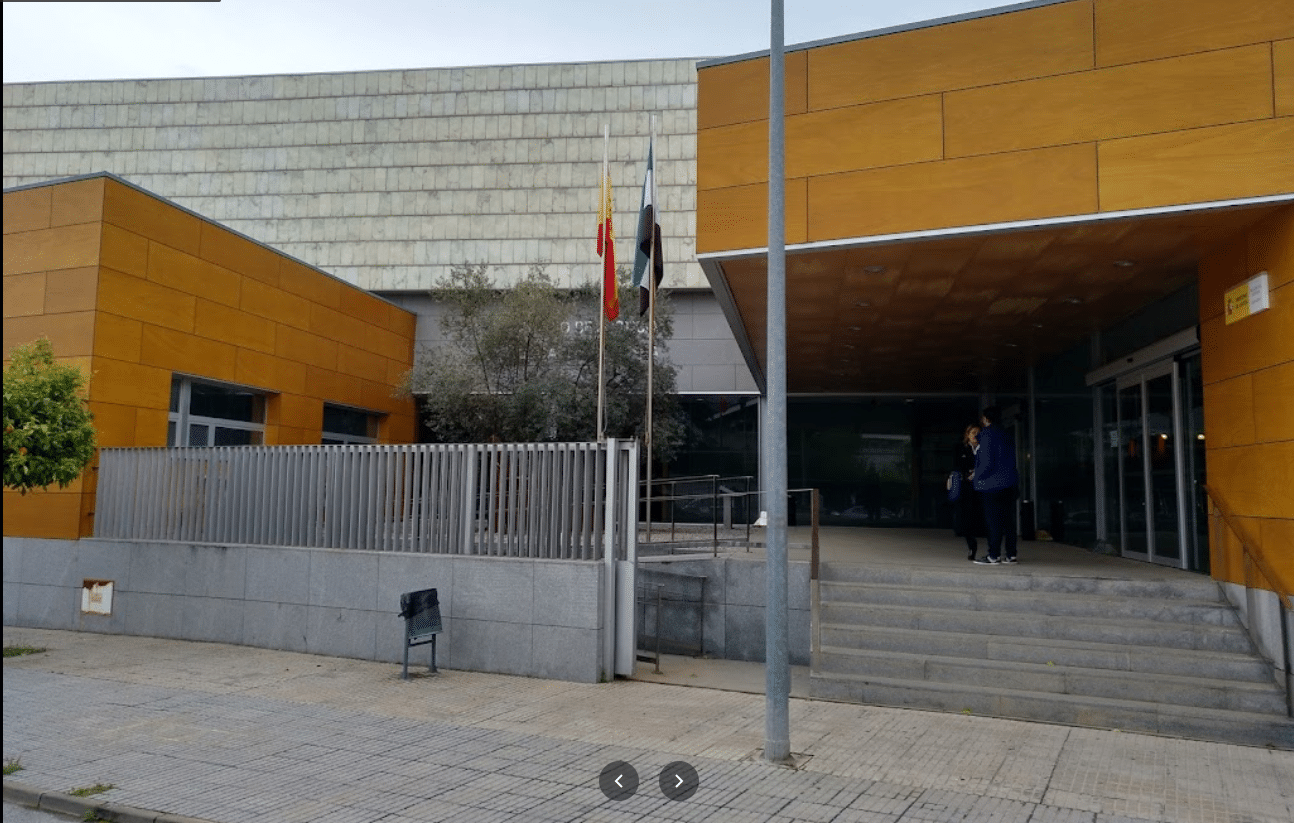 Entrada a un edificio de paredes amarillas con banderas españolas, escalones y gente oculta.