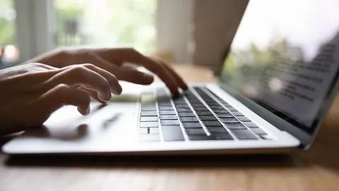 Manos escribiendo en un teclado de computadora portátil, primer plano, en el interior.
